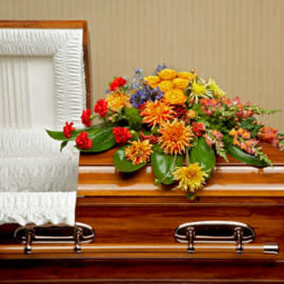 Bright mixed spray of yellow and orange flowers arranged on a wooden casket with white interior