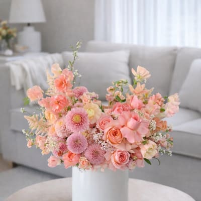 Pink and peach floral arrangement in a white vase on a table