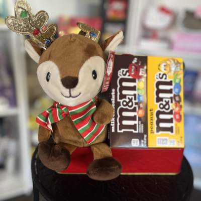 Plush reindeer with a striped scarf beside two M&M's candy boxes