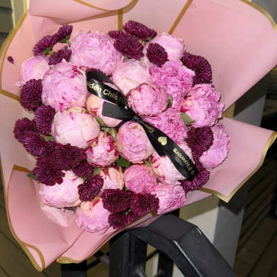 Pink bouquet of peonies and dark purple chrysanthemums wrapped in pink paper