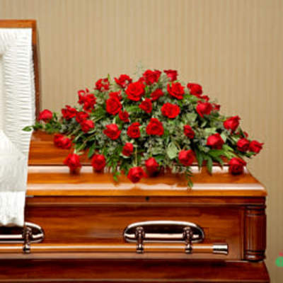 Red rose casket spray on a polished wood casket with white interior