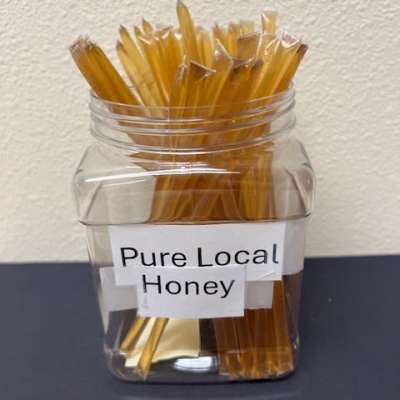 Clear jar filled with honey sticks labeled Pure Local Honey