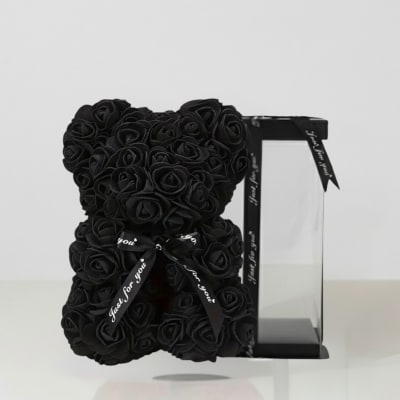 Black rose teddy bear beside a clear display box with ribbon