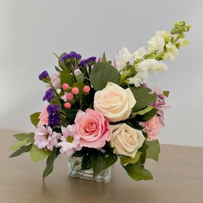 Pink and cream roses in a clear square vase with purple and white accent flowers