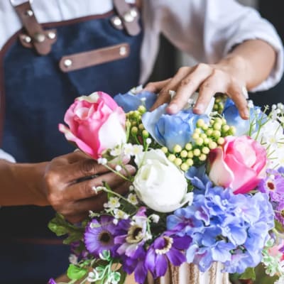 Person arranging pink, white, and blue flowers in a vase