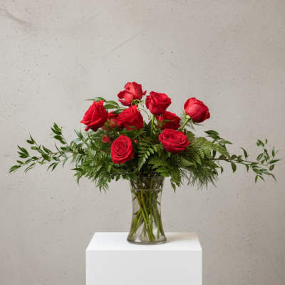 Red roses arranged in a clear glass vase with greenery
