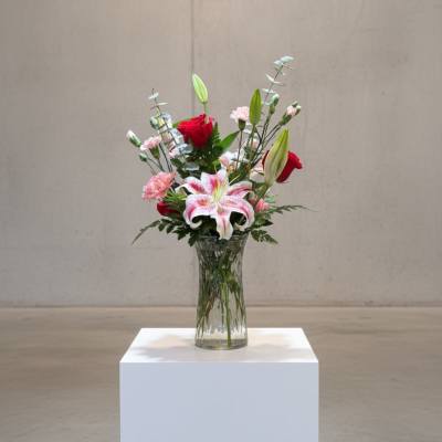 Mixed bouquet with lilies and red roses in a clear glass vase