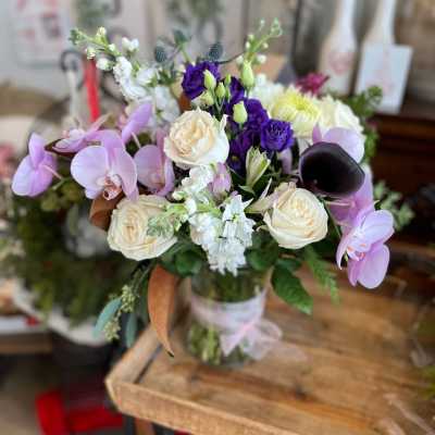 Mixed bouquet with lavender orchids, cream roses, and purple blooms in a glass vase
