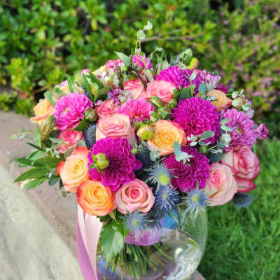 Bouquet of pink and peach roses with purple blooms in a glass vase