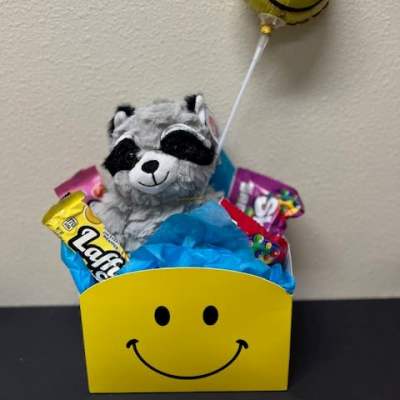 Gift basket with a plush raccoon, candy, and a smiley balloon
