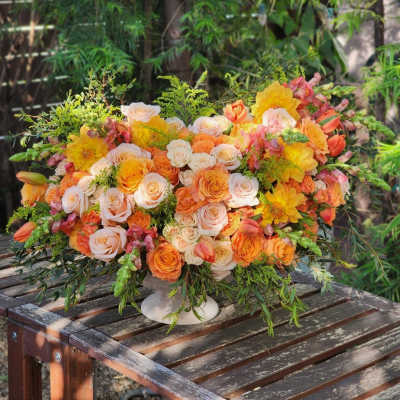 Large bouquet of peach, orange, and yellow flowers in a white pedestal vase