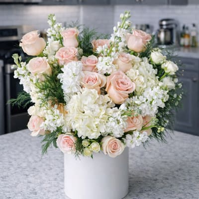 Blush roses and white flowers arranged in a white vase