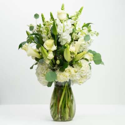 White floral arrangement in a glass vase with green accents