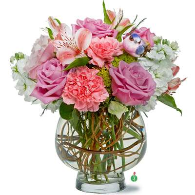 Pink and white mixed bouquet with roses and carnations in a round glass vase with curly branches