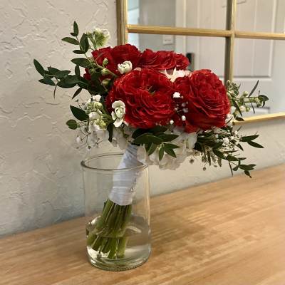 Hand-tied bouquet of red and white flowers resting in a clear glass vase.