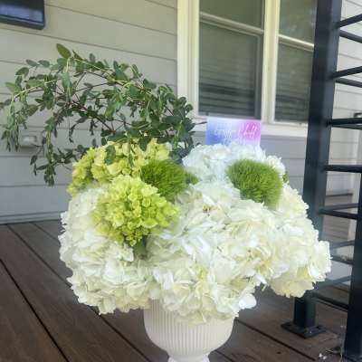White and lime-green floral arrangement in a white pedestal vase