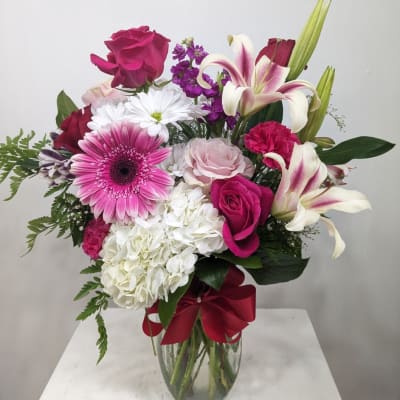 Mixed bouquet of pink and white flowers in a glass vase with a red ribbon