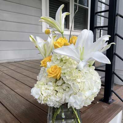 White lilies and yellow roses arranged in a clear glass vase