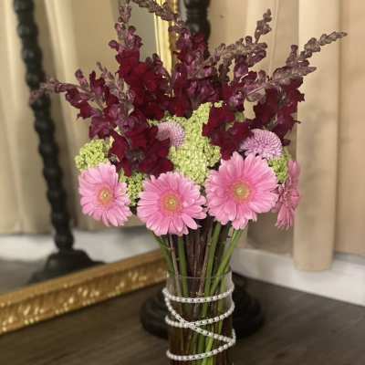 Pink gerbera daisies and burgundy snapdragons in a clear vase with pearl wrap