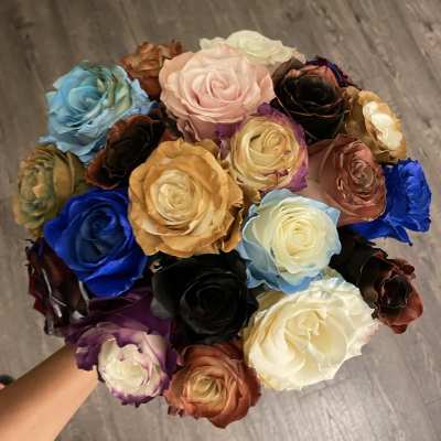 A hand holds a bouquet of multicolored roses.