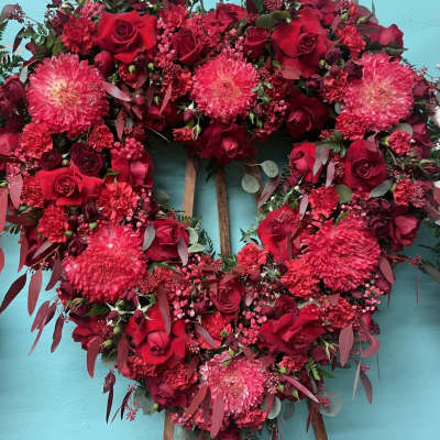 Heart-shaped floral wreath of red roses and pink blooms on a stand