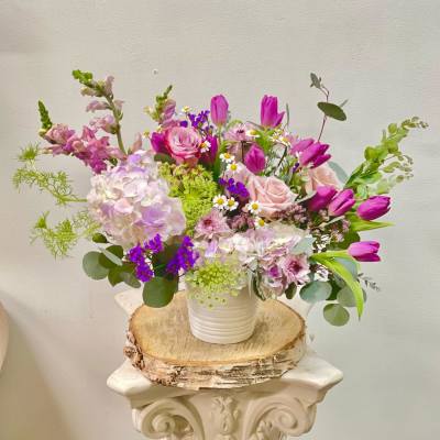 Mixed pink and purple flowers in a white vase on a wood slice