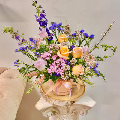 Pastel roses and purple flowers arranged in a pink hat box