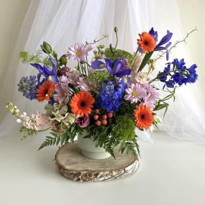 Colorful mixed flower arrangement in a white vase on a wood slice base