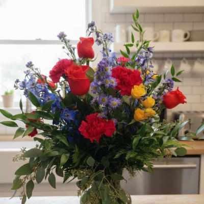 Mixed bouquet of red, yellow, and blue flowers in a glass vase