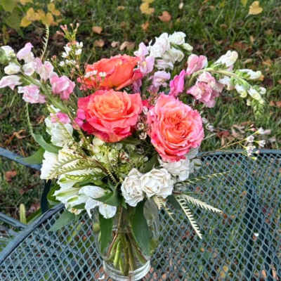 Pink and coral roses in a clear glass vase with white accent flowers