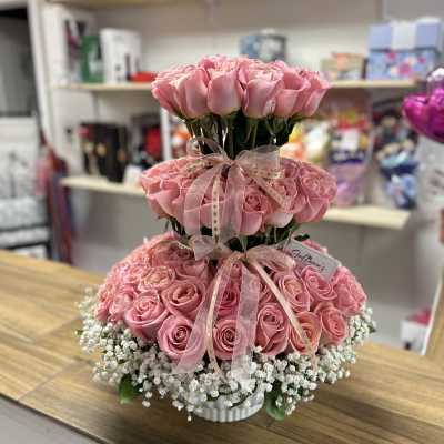 Tiered arrangement of pink roses with white baby's breath in a white container