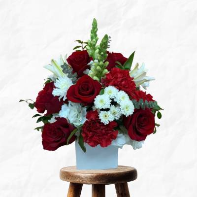 Red roses and white flowers arranged in a light blue box on a stool
