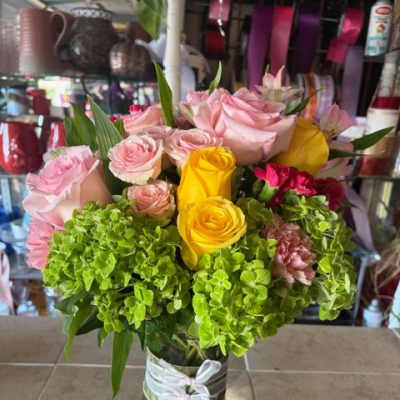 Pink and yellow roses in a clear glass vase with green hydrangeas
