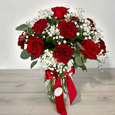 Red roses and carnations in a glass vase with baby's breath and a red ribbon