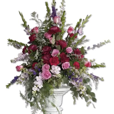 Tall pink and purple floral arrangement in a white pedestal vase