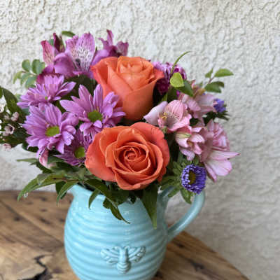 Bouquet of orange roses and purple daisies in a blue ceramic pitcher