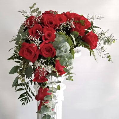 Red roses arranged in a tall white vase with trailing greenery