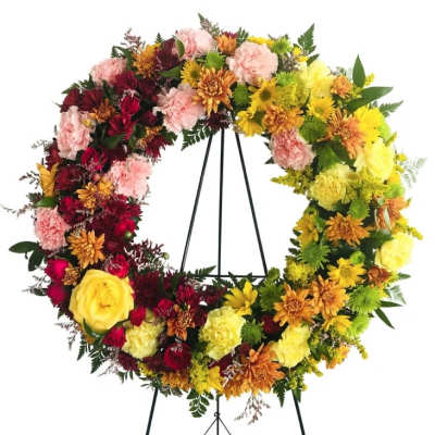 Large floral wreath on a black stand with red, pink, yellow, and orange blooms