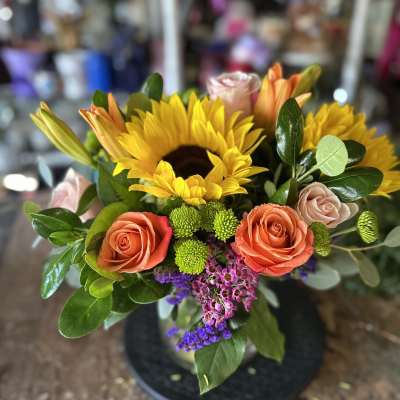 Bouquet of sunflowers, roses, and lilies in a black vase