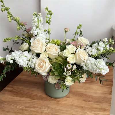 Cream roses and white flowers arranged in a green vase