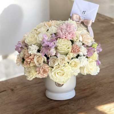 Pastel bouquet of roses and carnations in a white vase with a ribboned card