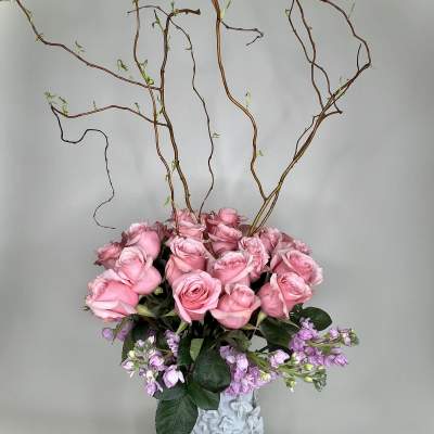 Pink roses in a white vase with tall curly branches