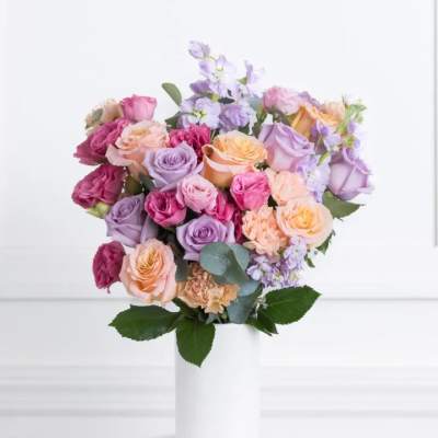 Bouquet of pastel roses and lavender flowers in a white vase