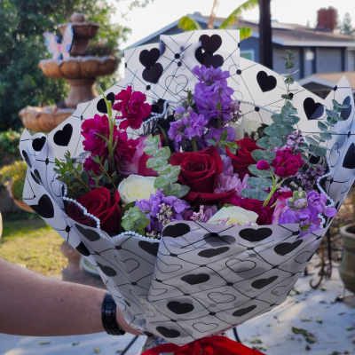 Bouquet of red, white, and purple flowers wrapped in heart-patterned paper