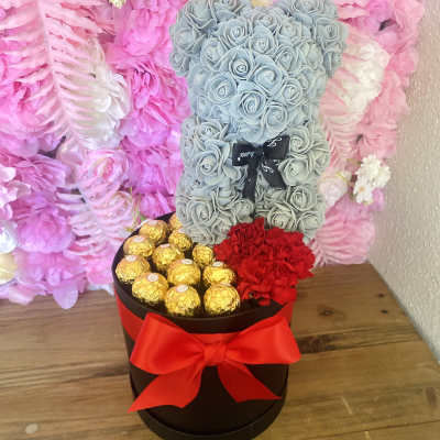 Blue teddy bear made of roses in a gift box with chocolates and a red bow