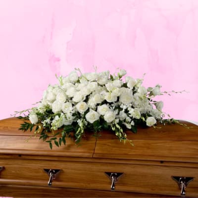 White rose casket spray on a light wood casket against a pink background