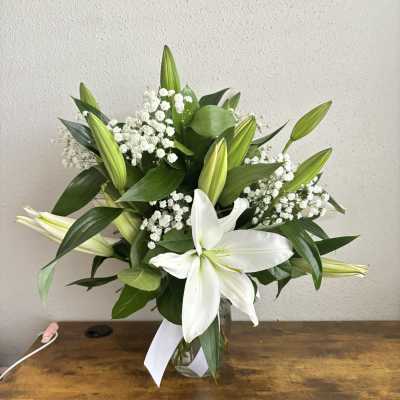 White lilies and baby's breath in a glass vase with a white ribbon