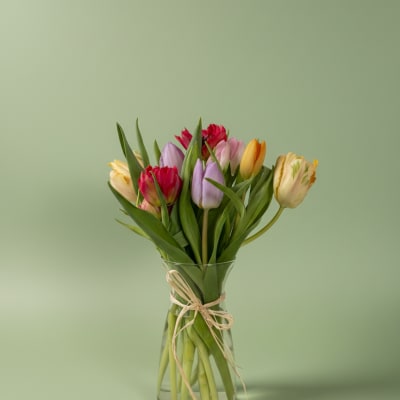 Mixed bouquet of colorful tulips in a clear glass vase tied with twine on a light green background