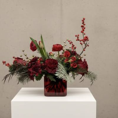 Red floral arrangement in a square glass vase with berries and greenery