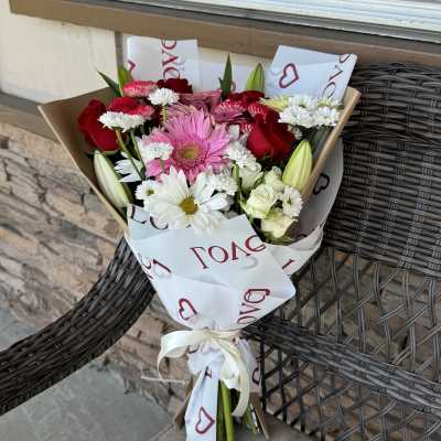 Bouquet of pink, red, and white flowers wrapped in paper with a ribbon